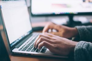 Person typing on laptop with another screen in the background.