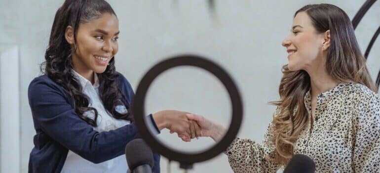 Women shaking hands in recording studio - everything is easier after you find influencers for your business.
