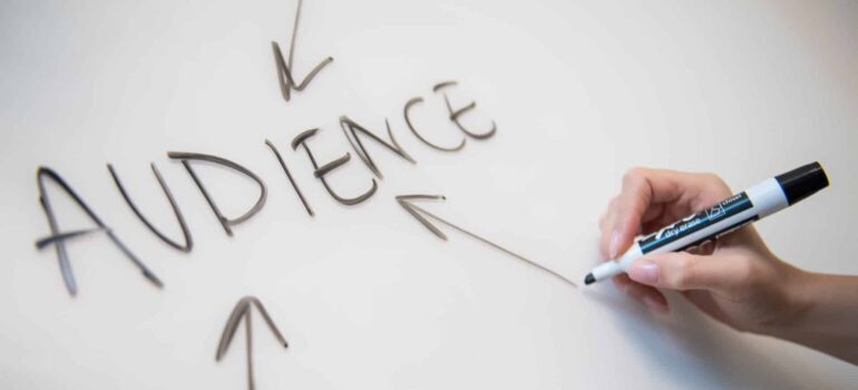 A man draws arrows to the word "Audience" on a white board.