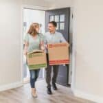 Two people carrying boxes into an empty house